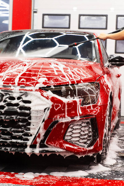 High-pressure water to flush foam. Paint-safe foam rinse removes foam. Red sports car detailing rinses thick snow foam with high-pressure water, removing dirt and leaving a streak-free, glossy finish