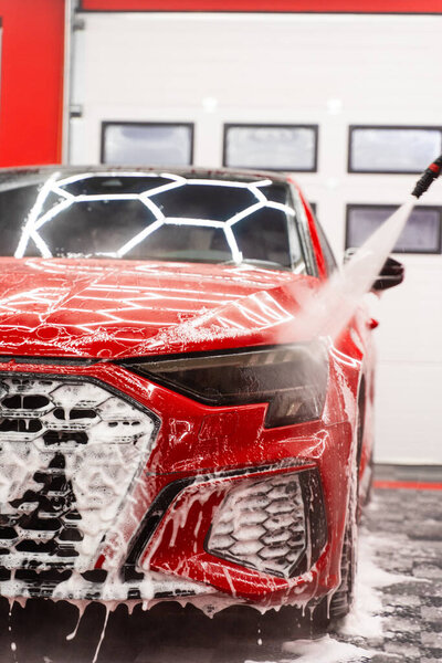 Red sports car detailing rinses thick snow foam with high-pressure water, removing dirt and leaving a streak-free, glossy finish. High-pressure water to flush foam. Paint-safe foam rinse removes foam