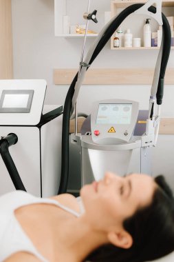 Kadın yenilenme seansından önce lazer ameliyatını bekliyor. Uzman olarak lazer sisteminin yanında sakince uzanan kız lazer prosedürü için cihazı hazırlıyor.