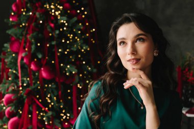 Noel hediyesini aklında tutan kadın Noel ağacı ve yılbaşı ışıklarıyla gülümsüyor.