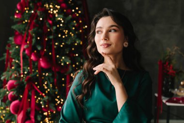 Gülümseyen kadın yılbaşını kutlamak için süslenmiş ağacın Noel hediyesini hayal ediyor.