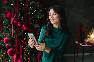 Noel ve yeni yıl partisinde elinde telefonla gülümseyen bir kadın.