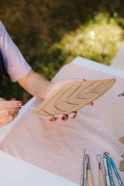 Esnaf, üzerinde ayrıntılı çizgiler olan bir kil yaprak oyar. Clay Leaf 'i oyan kadın. Genç bir kadın çömlekçilik yeteneklerini sergilemek için kilden ince yaprak desenleri oyuyor.
