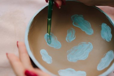 Mavi desenli seramik kasede pigment ve fırça kullanılıyor. Fırça kullanarak mavi pigmentli seramik kase boyamak. Seramik kâse dekorasyonu boyama süreci ve çömlek tekniğini vurguluyor