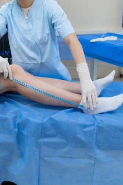 Damar doktoru bacağının ölçüsünü şeritle ölçüyor.