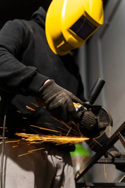 İşçi, sarı bir kaskla metal kesiyor.