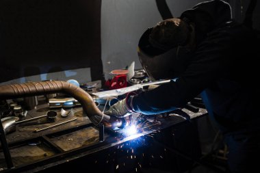 İşçi SMAW kaynak yapıyor. Çeliğe koruyucu miğfer ve kıvılcımlar takıyor.
