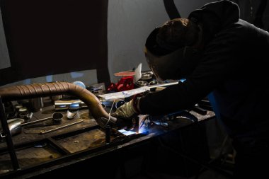 Kaynak miğferindeki işçinin kalkanlı metal yay işlemiyle kaynaklama.