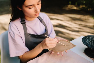 Clay Leaf 'i oyan kadın. Genç bir kadın çömlekçilik yeteneklerini sergilemek için kilin içine ince yaprak desenleri oyuyor. Sanatçı, ayrıntılı çizgileri olan bir kil yaprağını oyuyor