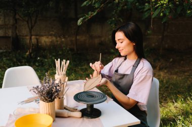 Clay Leaf 'i oyan kadın. Genç bir kadın çömlekçilik yeteneklerini sergilemek için kilin içine ince yaprak desenleri oyuyor. Sanatçı, ayrıntılı çizgileri olan bir kil yaprağını oyuyor
