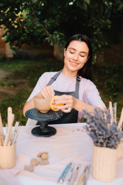 Clay Bowl 'u şekillendiren genç kadın. Potter, tekerleğinde sünger olan, şekil ve dokuları rafine eden bir kir kabını yumuşatır. Sanatçı kilden bir kase üzerinde dikkatle çalışır, şeklini süngerle düzeltir.
