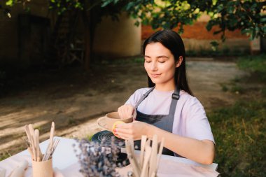 Clay Bowl 'u şekillendiren genç kadın. Potter, tekerleğinde sünger olan, şekil ve dokuları rafine eden bir kir kabını yumuşatır. Sanatçı kilden bir kase üzerinde dikkatle çalışır, şeklini süngerle düzeltir.