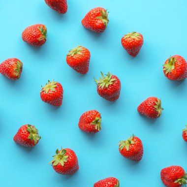 Mavi arka plana serpilmiş taze çilekler.
