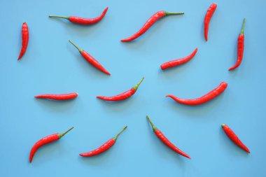 Kırmızı biberler mavi arkaplanda dizilmiş.