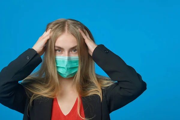 Yüzünde tıbbi maske olan bir iş kadını kafasını tutuyor.