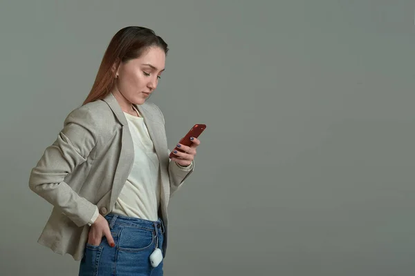 Söt flicka med en telefon i händerna på en grå bakgrund — Stockfoto