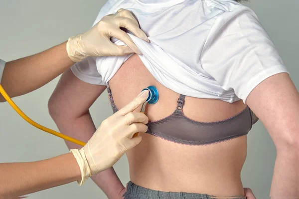 Doktor resepsiyondaki hastayı fonendoskopla dinliyor.