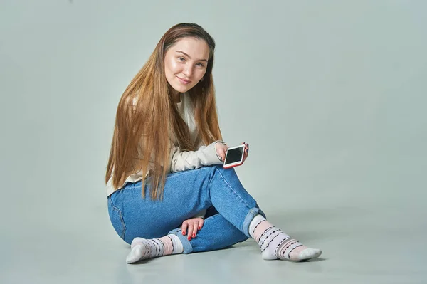 Arka planda oturan bir kız elinde telefonla gülümsüyor.