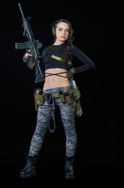 Tüfekli genç bir kadın siyah arka planda duruyor.