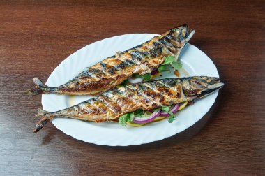 Izgarada pişmiş uskumru beyaz bir tabakta yatıyor.