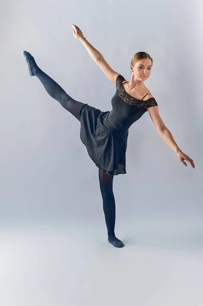 De ballerina staat op de achtergrond en heeft haar been omhoog gebogen naar de vloer — Stockfoto