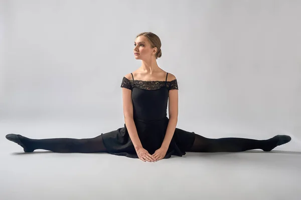 Ballerina sits in a cross splits on the background in a black swimsuit — Stock Photo, Image
