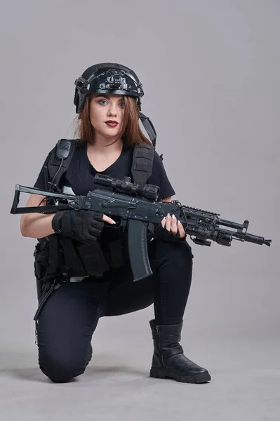 若い女性は灰色の背景に彼女の手に機関銃で座っています — ストック写真