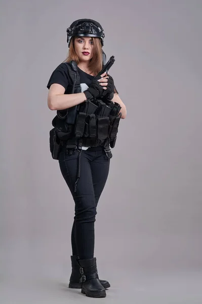 Mladá žena sedí s pistolí v rukou na šedém pozadí — Stock fotografie