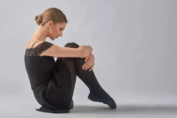 A bailarina senta-se no fundo com as pernas enfiadas no peito — Fotografia de Stock