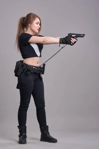 Une jeune femme tient un pistolet à bout de bras sur un fond gris — Photo