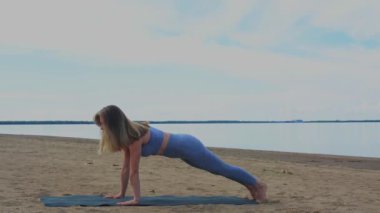 Sahilde nehrin arka planında bir kadın ısınıyor, yoga yapıyor.