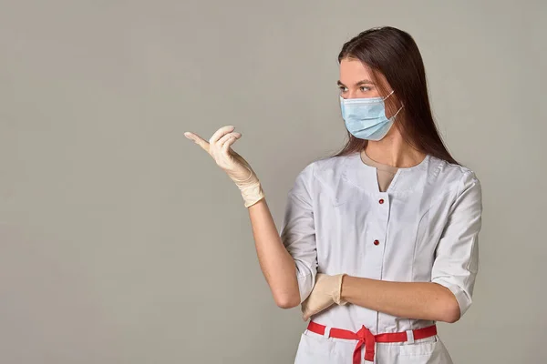 A female doctor in a medical mask points to an empty place, copy space — Stock Photo, Image