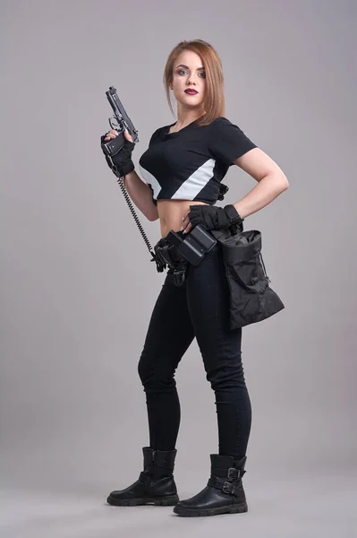 Mladá krásná žena stojí na šedém pozadí se zbraní v rukou — Stock fotografie