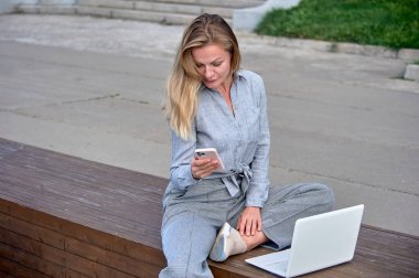 Dizüstü bilgisayarı olan bir kadın ahşap bir platformda oturuyor ve internette çalışıyor.