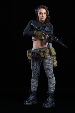 Genç bir kadın siyah arka planda bir tüfekle duruyor.