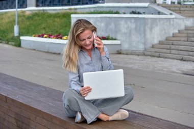 Dizüstü bilgisayarı olan bir kadın ahşap bir platformda oturuyor ve internette çalışıyor.
