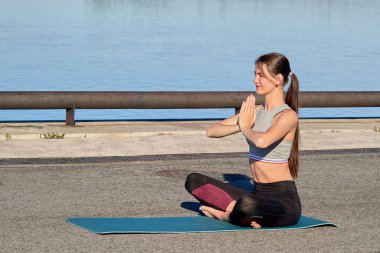 Genç bir kadın sabahın erken saatlerinde iskelede ısınıyor, nehrin arka planına karşı.