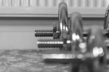 Arka plandaki en büyük ağırlığa odaklanan bir sıra halterin siyah beyaz fotoğrafı