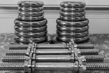 Evde yerde ağırlık kaldırma ekipmanlarının siyah beyaz fotoğrafı.