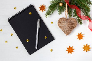 Noel 'de ve yeni yılda dilek listesi için siyah not defteri. Altın yıldızlarla süslenmiş beyaz ahşap arka planda marangoz kalbi ve ladin dalları yanında.