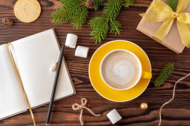 Noel sabahı konsepti, sarı kahve fincanı ve not defteriyle ahşap masaya sarılı bir hediye.