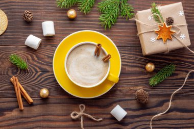 Sarı kapuçino ya da latte ile noel kompozisyonu ve ahşap masaya retro tarzında paketlenmiş hediye.
