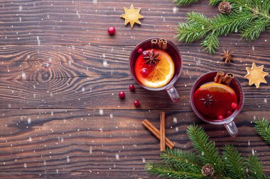 Sıcak Noel şarabı ve cam bardaklarda tarçın soğuk bir kar yağışı altında, kahverengi bir tahta masada.