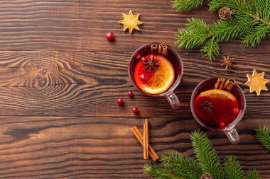 Noel şarabı tarçınlı ve portakallı, kahverengi ahşap bir masada, ladin dalları ve kızılcıkların yanında.