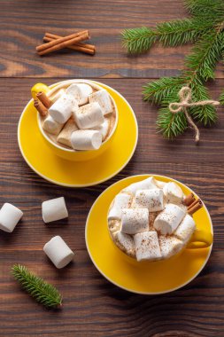 İki sarı kapuçino, marşmelov ve ahşap arka planda ladin dalları.