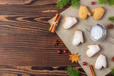 Koyu ahşap masa üzerinde pudra şekeri ve tarçın çubuklarıyla kabartma kağıdında Xmas bisküvileri