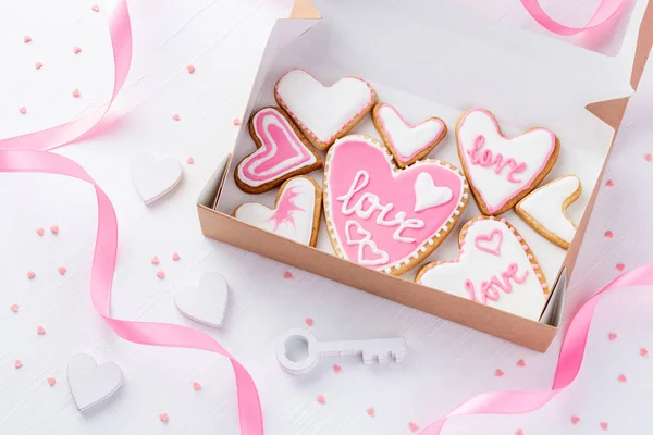 白い木のテーブルの上の鍵の近くに美しい言葉の愛を持つハート型のクッキーがいっぱいの箱バレンタインデー — ストック写真