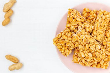 Geleneksel Hint fıstıklı chikki tabakta beyaz arka plan, üst manzara. Lohri festivali için beyaz ahşap masadaki şekerli fıstık ezmesi parçaları..