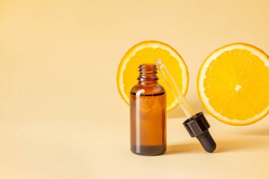 Vitamin cosmetics in glass bottle against flying orange slices on yellow background. Blank transparent brown vial with classic eyedropper. Natural perfume or fluid cosmetics for spa and skincare. clipart