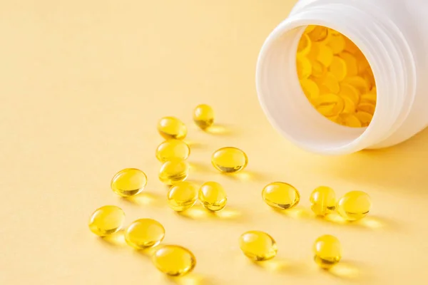 Soft gel supplement capsules with vitamin A and open bottle on yellow background, close-up